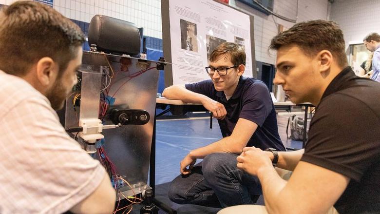 Three male students look at autonomous wheelchair